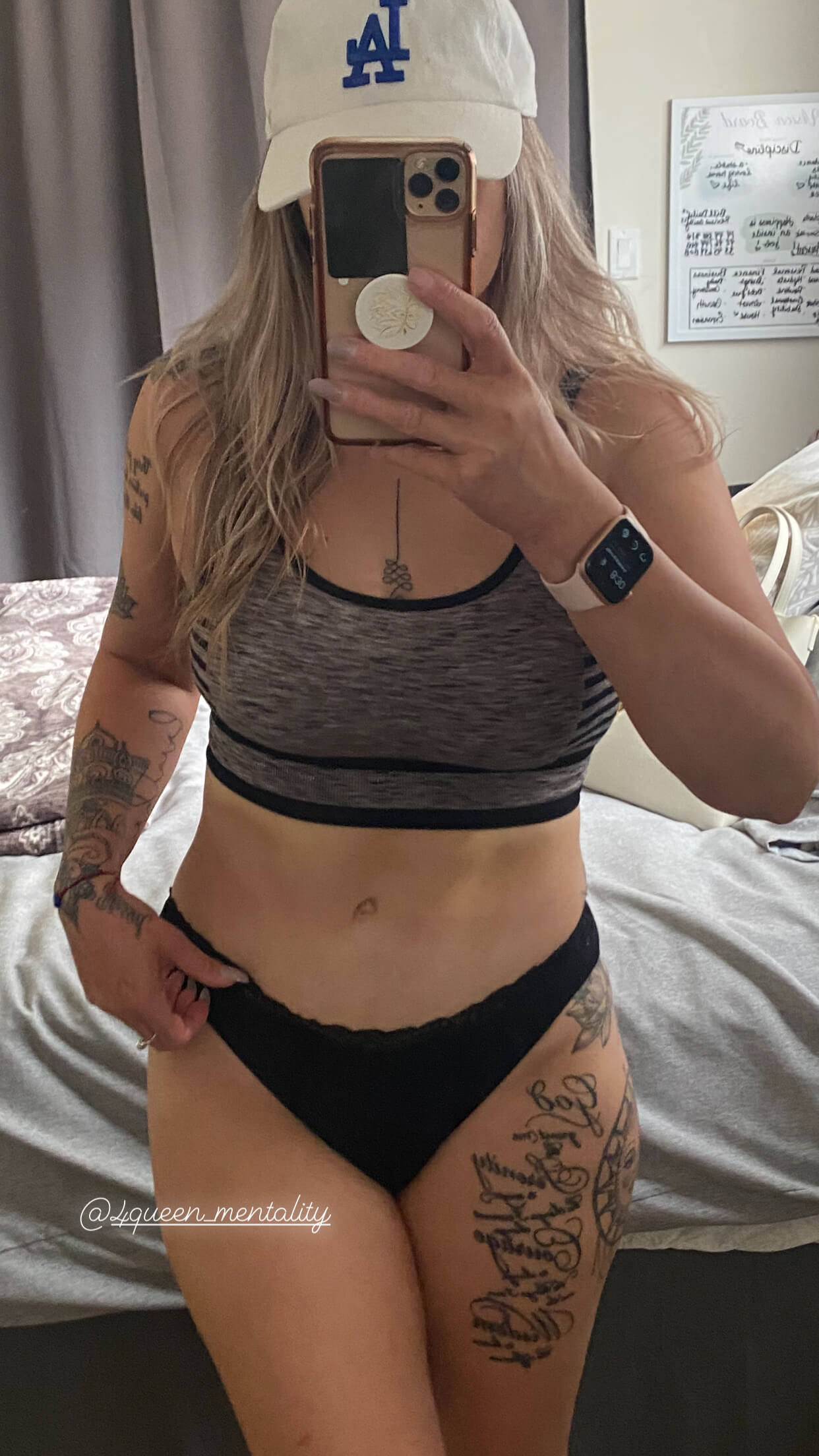 Fit woman in sportswear taking a mirror selfie showing toned abs and tattoos.