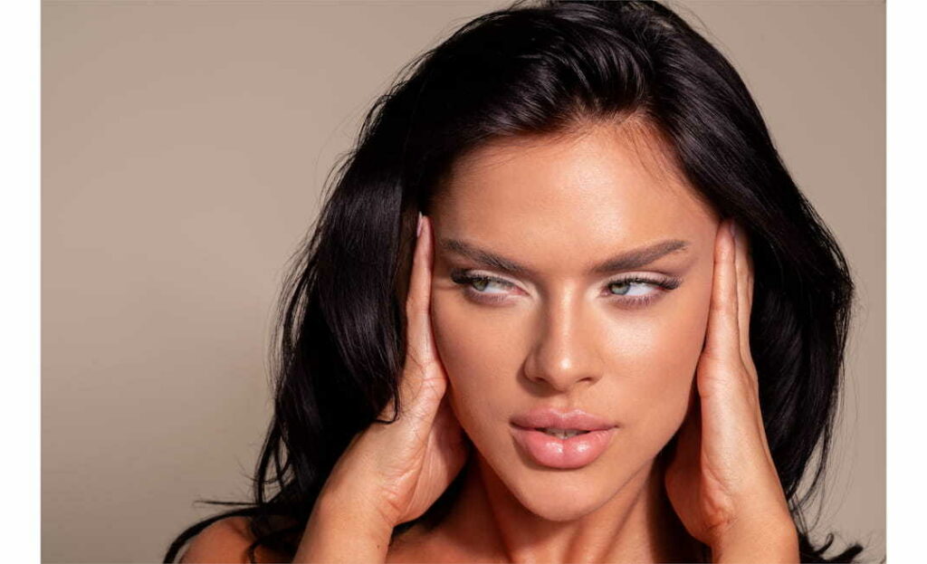 Close-up portrait of a woman showcasing a dramatic cat-eye makeup look with flawless skin and dark hair.