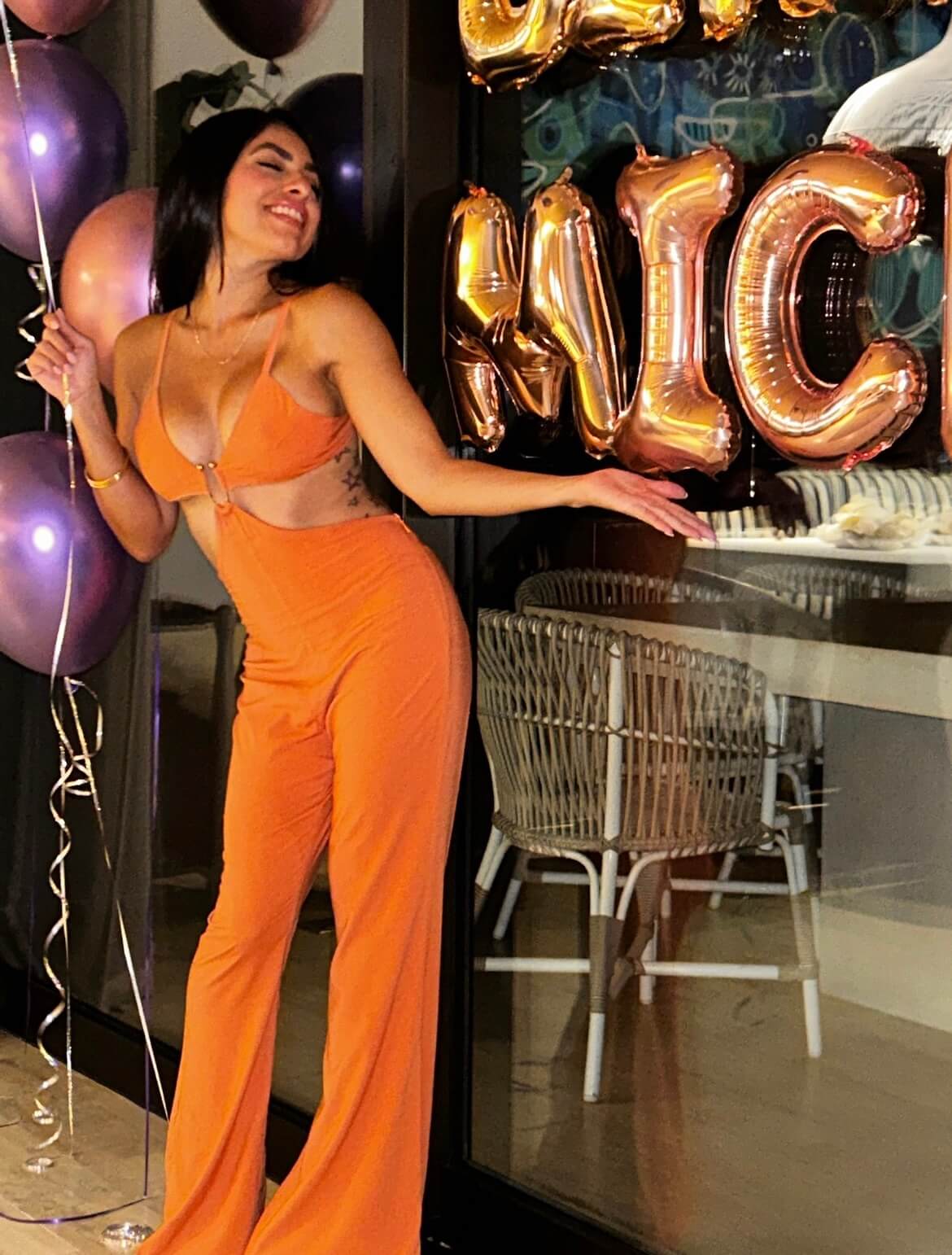 Cheerful woman in an elegant orange outfit smiling and posing with balloons.