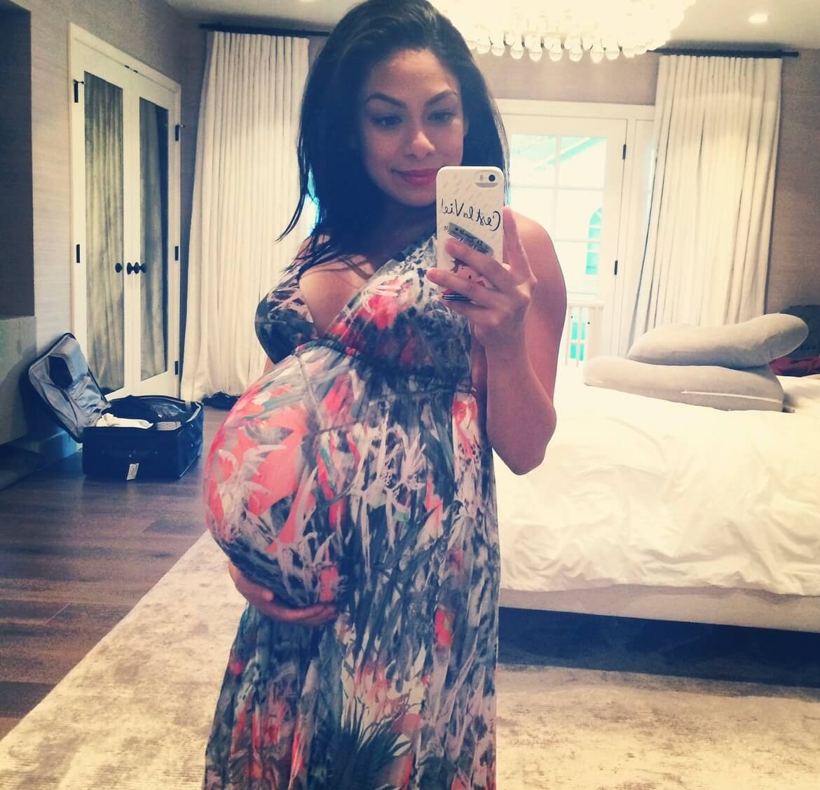 Pregnant woman taking a mirror selfie in a bedroom, wearing a colorful maxi dress