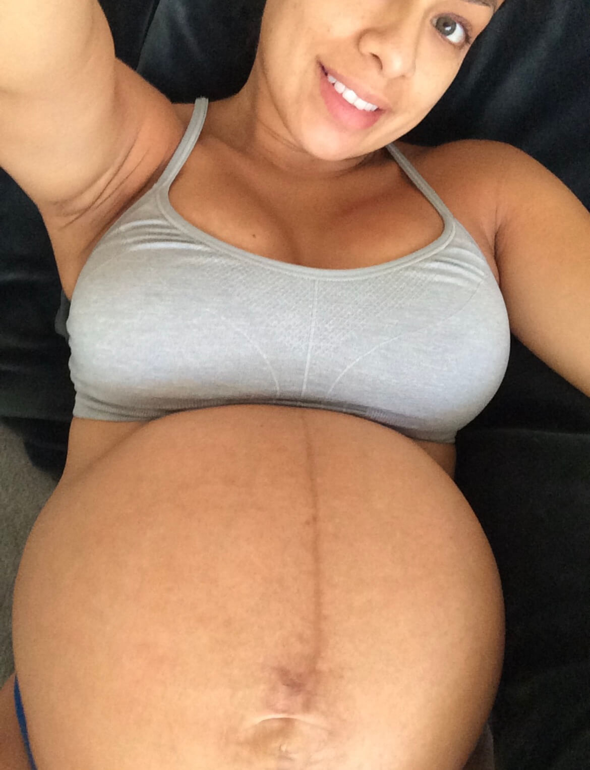 Pregnant woman in grey sports bra showing her belly before childbirth.