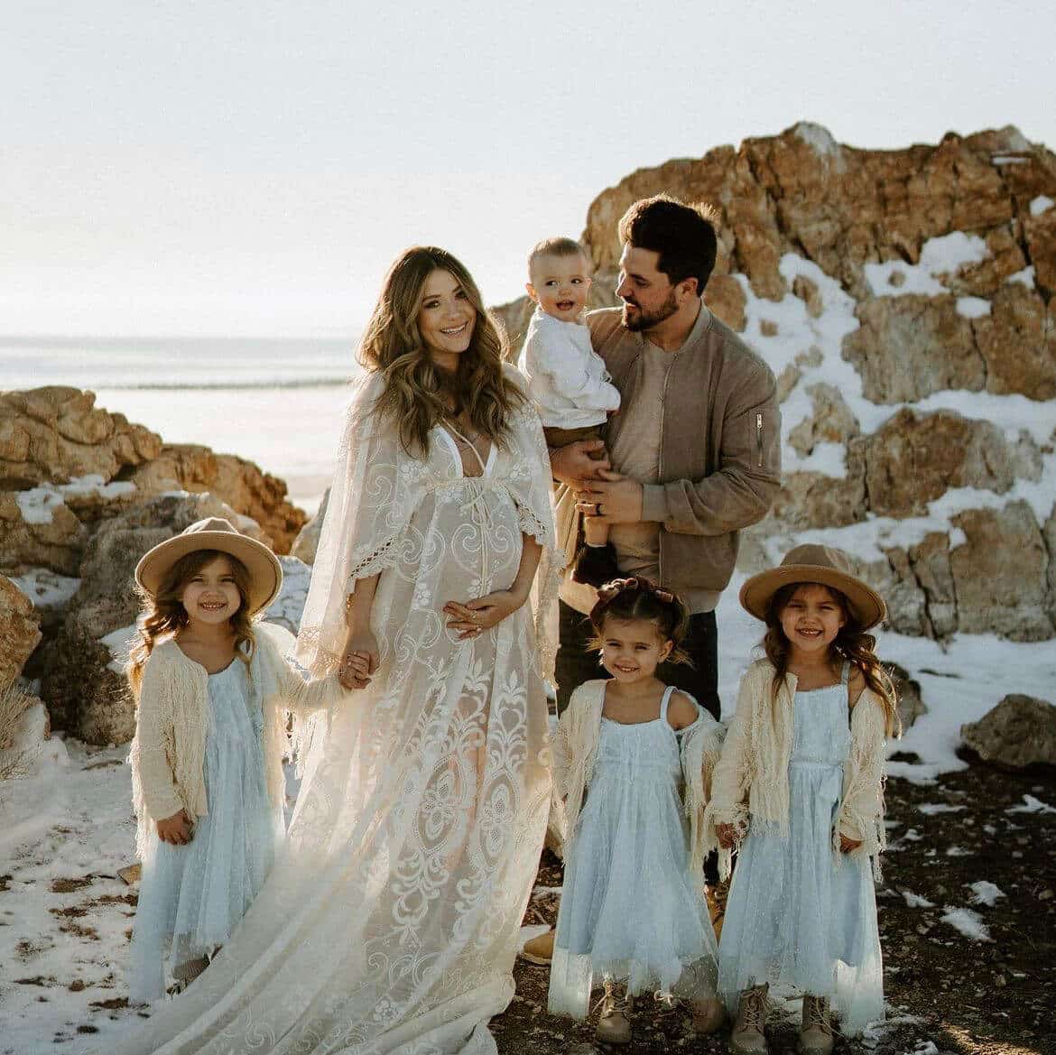 Happy family portrait on a beach, featuring parents and four children dressed elegantly, smiling together.