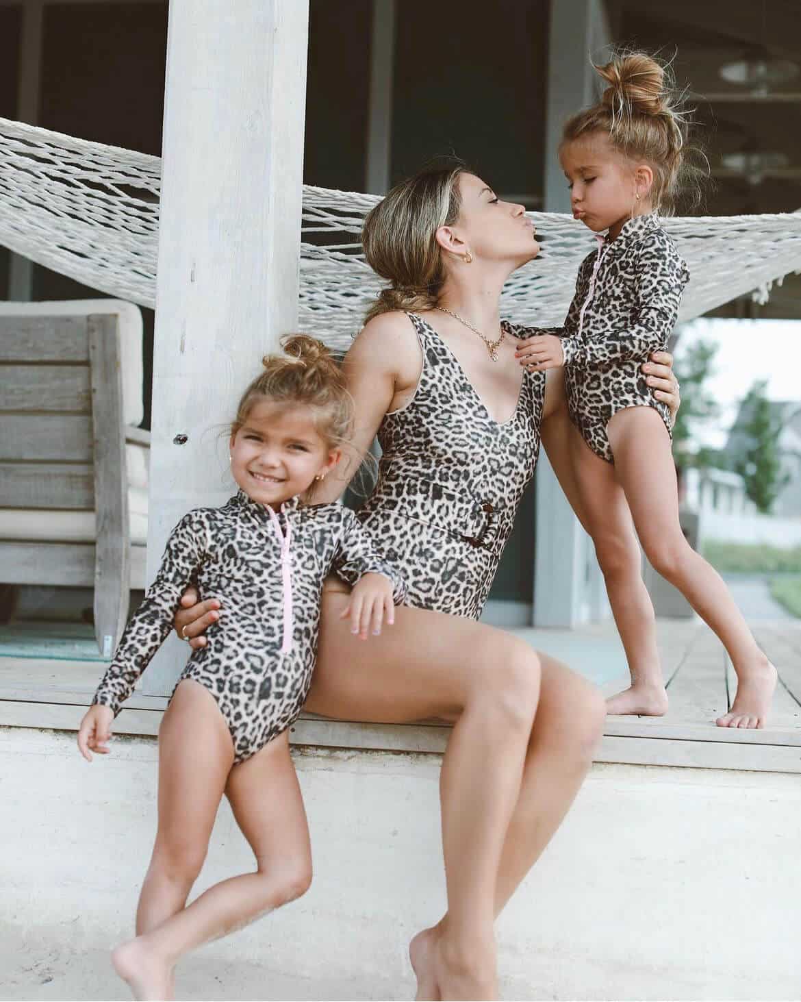 Happy mother and two young daughters wearing matching leopard-print swimsuits, enjoying playful family moments outdoors