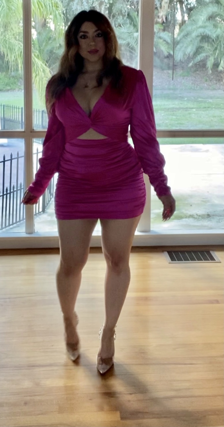 Woman confidently posing in a vibrant pink mini dress, highlighting her elegant silhouette, in front of a bright, spacious window.