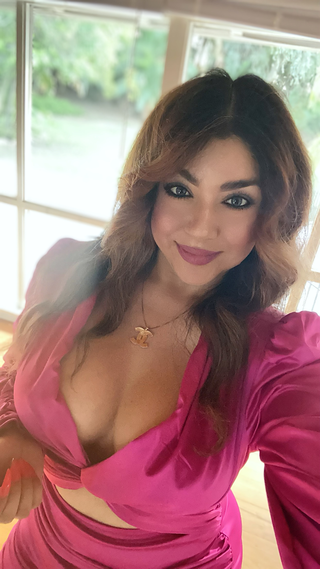 Smiling woman with voluminous hair wearing a vibrant pink dress, showcasing her post-surgery confidence.