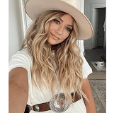 Smiling woman with long blonde wavy hair wearing a stylish hat and white dress.