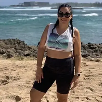 Smiling woman standing confidently on the beach wearing casual athletic clothing.