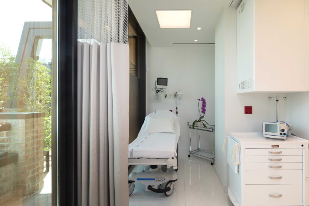 Recovery bay with a bed, patient monitor and a window onto the terrace at Dr. Cat Plastic Surgery