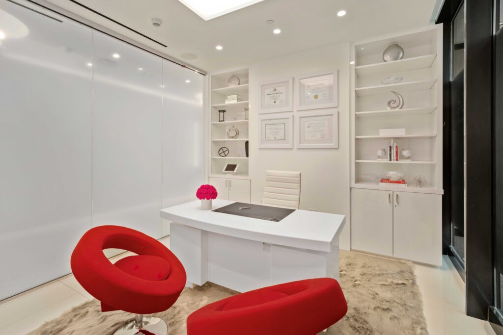 Private consultation room with a white desk and two red chairs at Dr. Cat Plastic Surgery