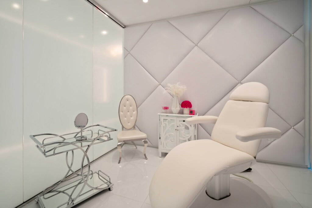 Chrome and glass exam room with a white reclining treatment chair and tufted walls
