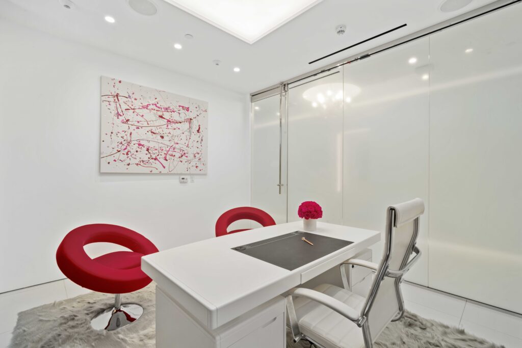 Consultation room with a white desk, red chairs and framed art