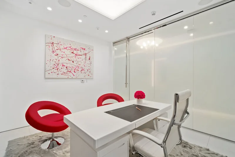 Consultation room at Dr. Cat Plastic Surgery with a white desk, red chairs and a pink splatter painting