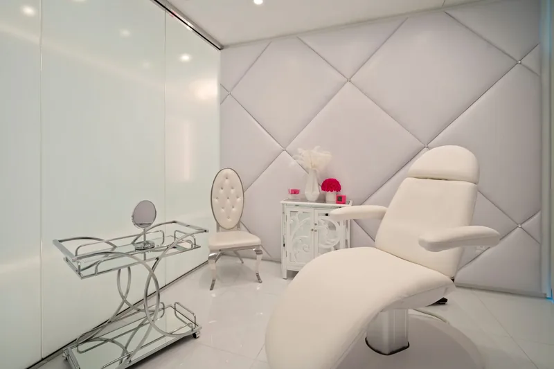 Exam room at Dr. Cat Plastic Surgery with a white treatment chair, chrome and glass finishes and tufted walls